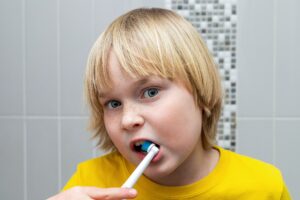 Child brushing teeth with electric toothbrush in bathroom